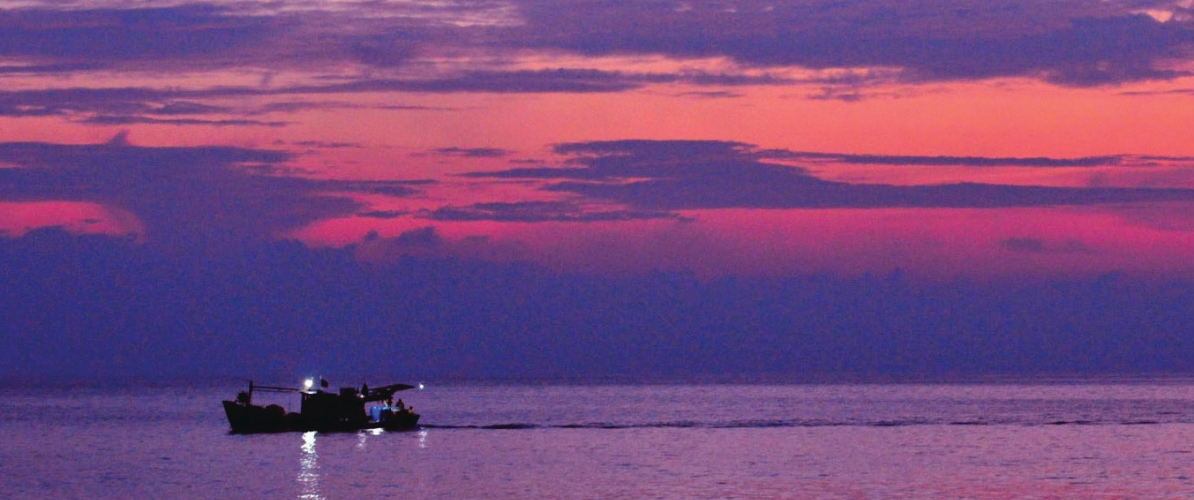 A fishing boat drifts across calm waters at sunset of the Johor islands' twilight sky