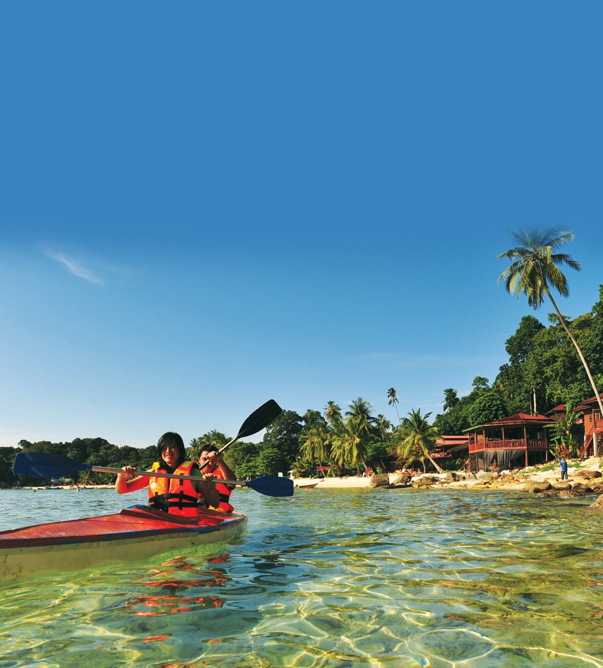 Two people kayaking in the crystal-clear waters near a tropical beach on Pulau Kapas or Pulau Lang Tengah